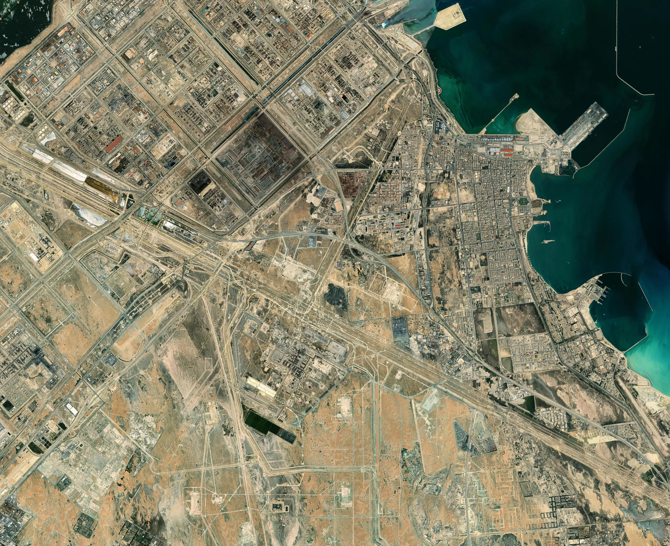 Real satellite imagery of a Saudi industrial and port city, refineries, port basin and dense urban blocks visible.
